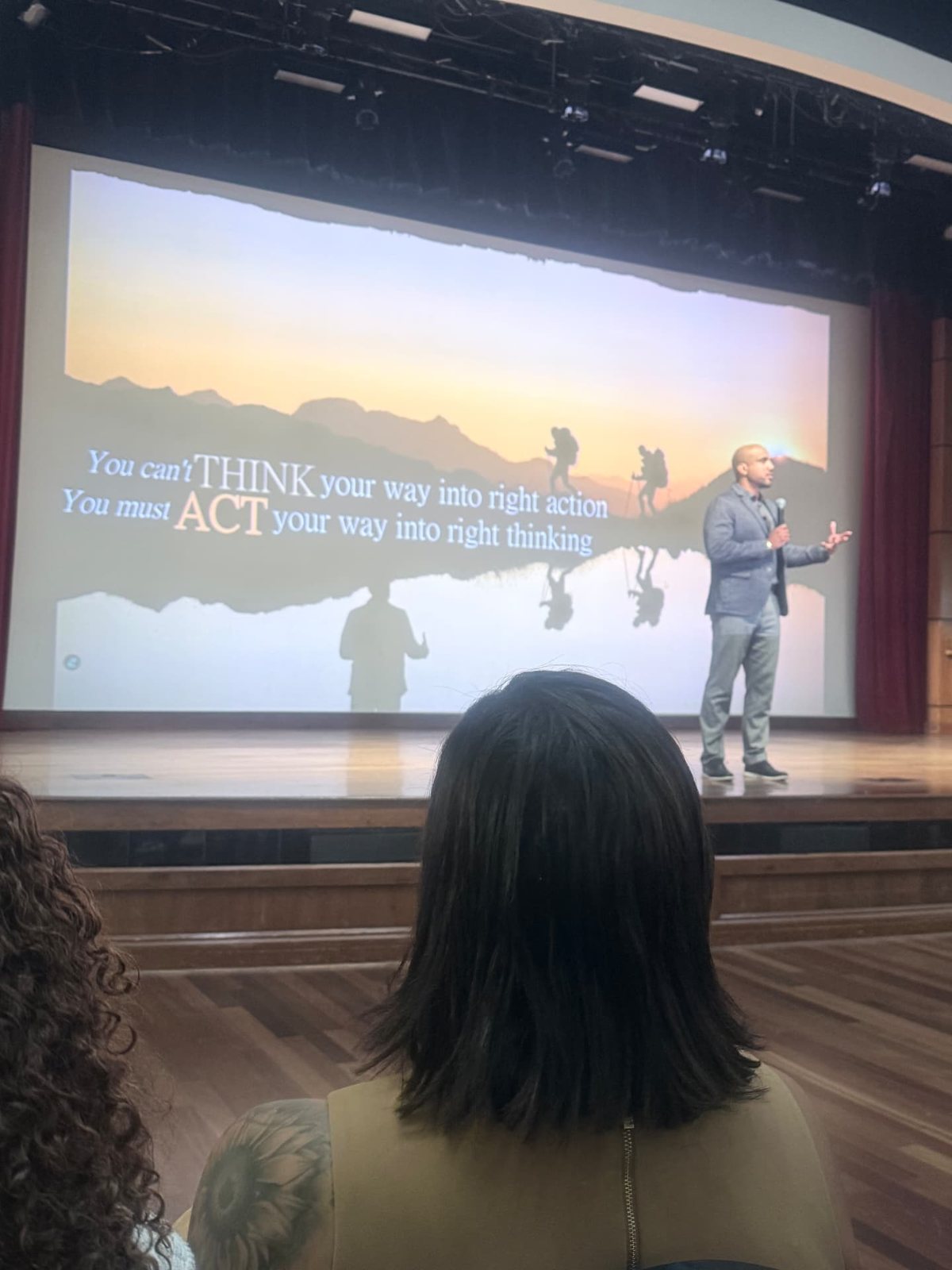 Arel Moodie on stage beside a slide reading You can't think your way into right action, you must act your way into right thinking