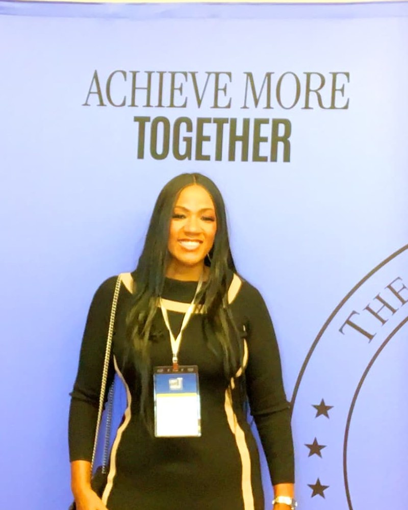Kimberly J. Lewis smiling in front of the summit backdrop reading Achieve More Together